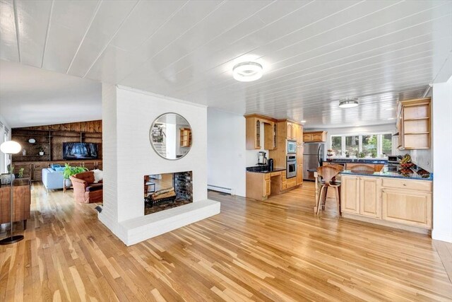 kitchen with light wood-type flooring, a brick fireplace, a baseboard radiator, and appliances with stainless steel finishes