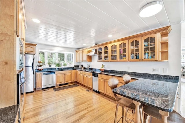 kitchen featuring appliances with stainless steel finishes, dark stone countertops, a kitchen bar, kitchen peninsula, and light hardwood / wood-style flooring