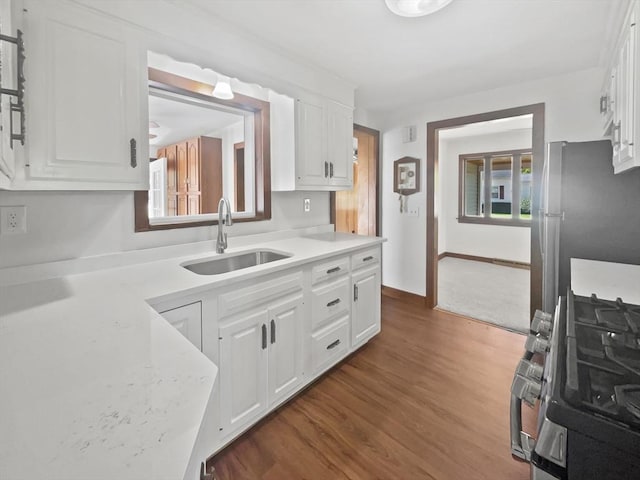 kitchen featuring white cabinets, appliances with stainless steel finishes, a sink, baseboards, and dark wood-type flooring