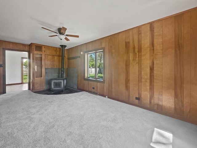 unfurnished living room with carpet, a ceiling fan, a wood stove, and wood walls