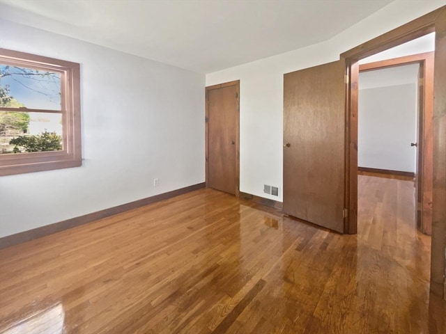 unfurnished bedroom with multiple closets, baseboards, visible vents, and wood finished floors