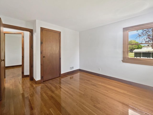 unfurnished bedroom featuring baseboards, a closet, wood finished floors, and visible vents