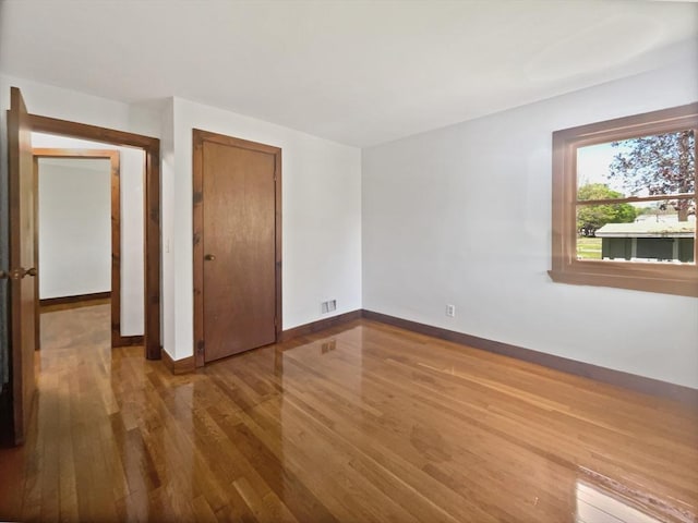 unfurnished bedroom with baseboards, wood finished floors, visible vents, and a closet