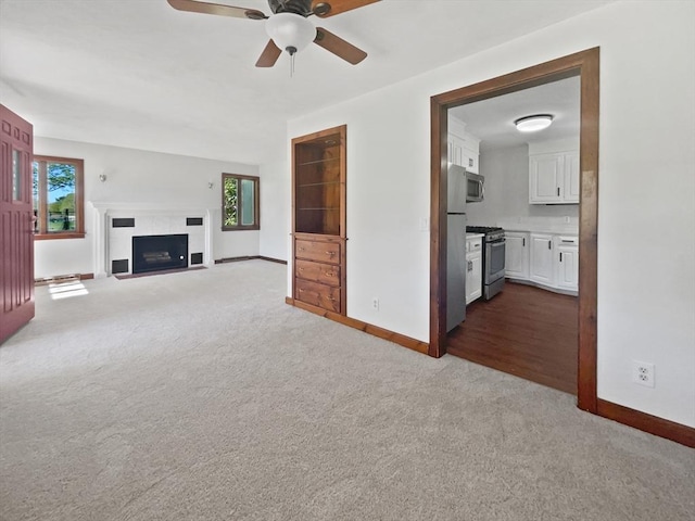 unfurnished living room with dark colored carpet, a ceiling fan, baseboards, and a healthy amount of sunlight