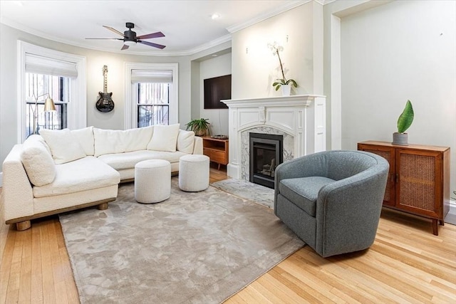 living room featuring hardwood / wood-style flooring, ceiling fan, ornamental molding, and a fireplace