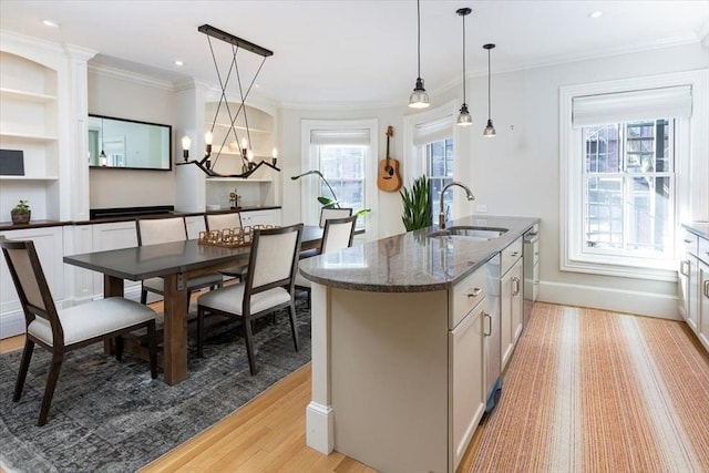 kitchen featuring sink, dark stone countertops, dishwasher, pendant lighting, and a kitchen island with sink