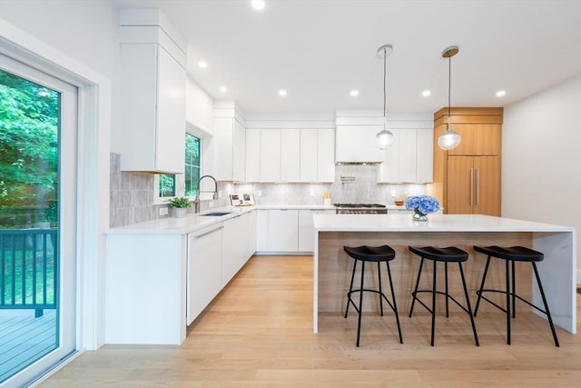 kitchen featuring light wood-type flooring, sink, white cabinets, a kitchen island, and hanging light fixtures