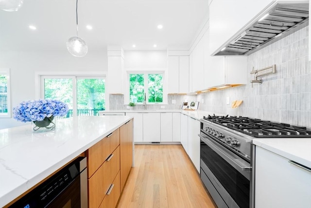 kitchen featuring white cabinets, stainless steel range with gas cooktop, decorative light fixtures, light stone counters, and custom range hood