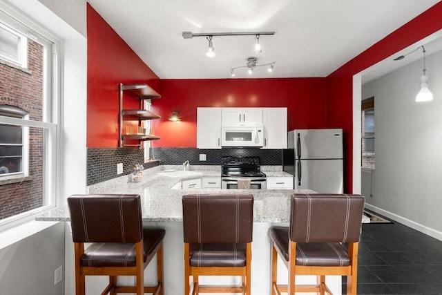 159 Cottage St Unit 6, Boston, MA 02128 - kitchen with stainless steel appliances, a peninsula, decorative backsplash, white cabinetry, and a kitchen bar