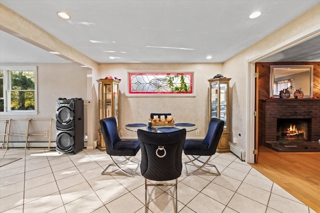 dining room with a baseboard radiator, a brick fireplace, and light wood-type flooring