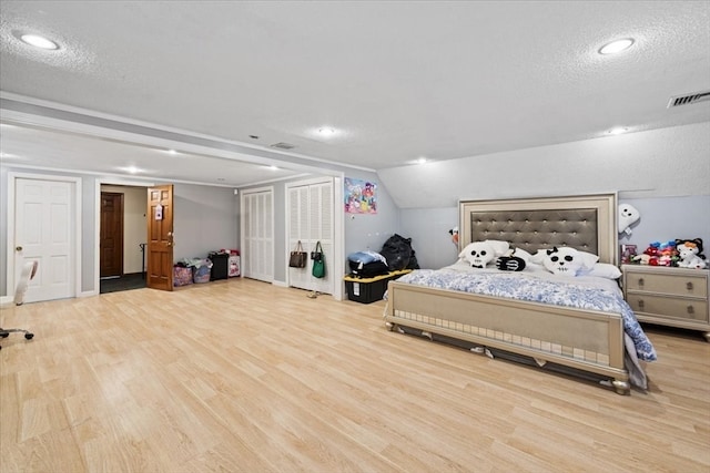 bedroom with vaulted ceiling, a textured ceiling, and light hardwood / wood-style flooring