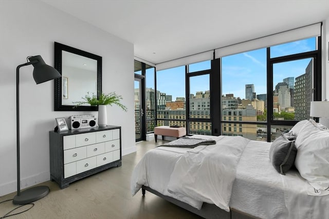 bedroom featuring a skyline view, light wood-style flooring, expansive windows, and baseboards