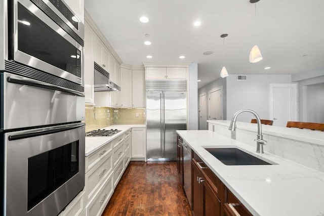 kitchen featuring visible vents, backsplash, a sink, built in appliances, and under cabinet range hood