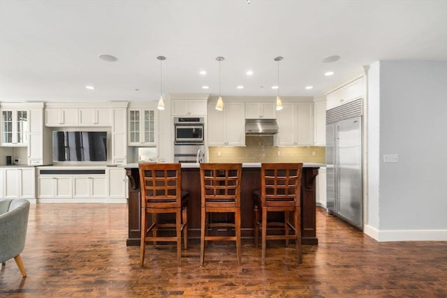 kitchen featuring white cabinets, decorative backsplash, an island with sink, stainless steel appliances, and under cabinet range hood