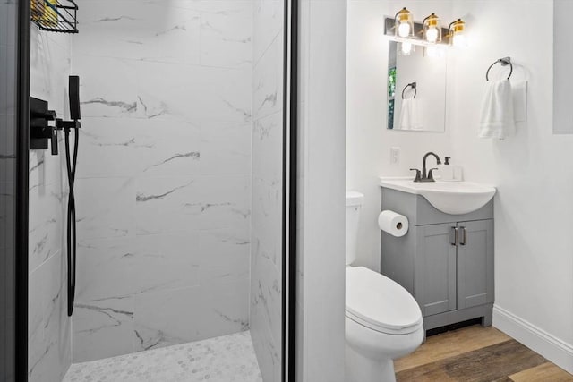 bathroom featuring toilet, a marble finish shower, wood finished floors, baseboards, and vanity