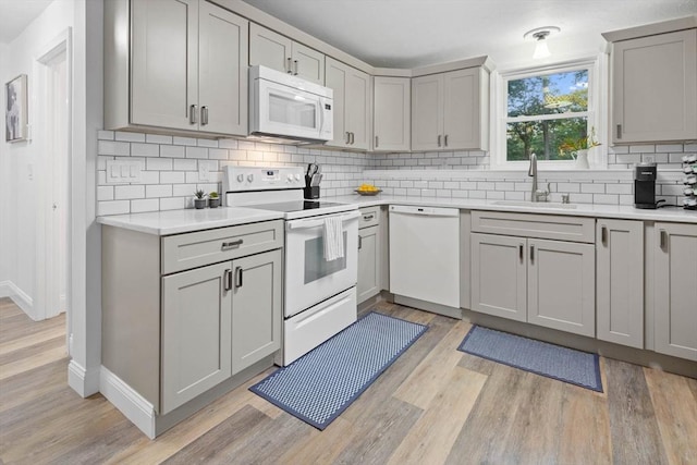 kitchen featuring a sink, white appliances, gray cabinets, and tasteful backsplash