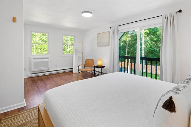 bedroom with multiple windows, access to outside, wood finished floors, and a baseboard heating unit