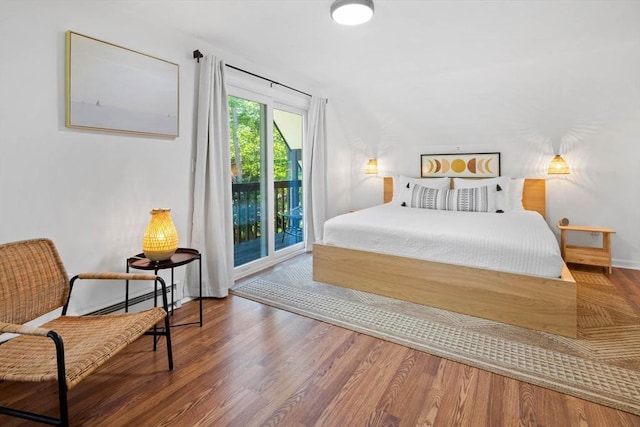 bedroom with baseboards, wood finished floors, a baseboard heating unit, and access to exterior