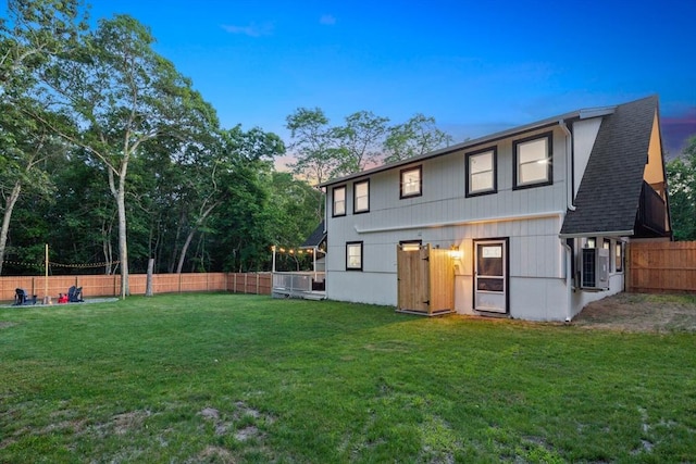 rear view of house with a shingled roof, fence, and a lawn
