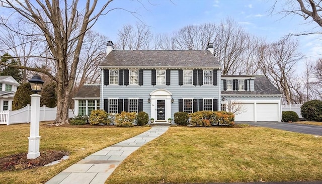 colonial inspired home with a garage, a front lawn, a chimney, and fence