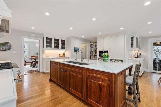 kitchen featuring light wood finished floors, a sink, stainless steel oven, and white cabinetry