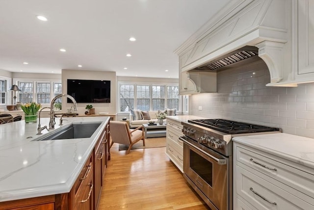 kitchen with light stone counters, high end stove, a sink, light wood-style floors, and open floor plan