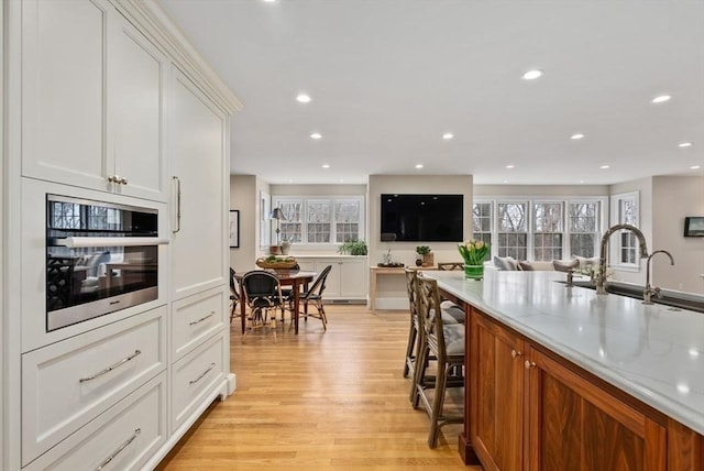 kitchen with recessed lighting, white cabinetry, stainless steel oven, light stone countertops, and light wood-type flooring