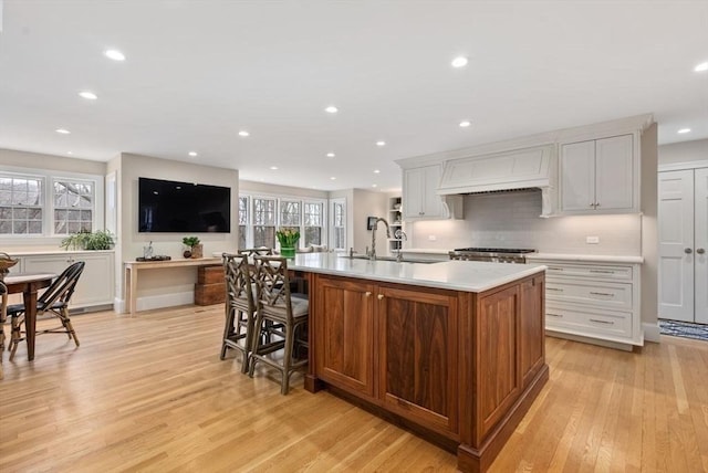 kitchen featuring a center island with sink, light countertops, custom range hood, light wood-style flooring, and a sink