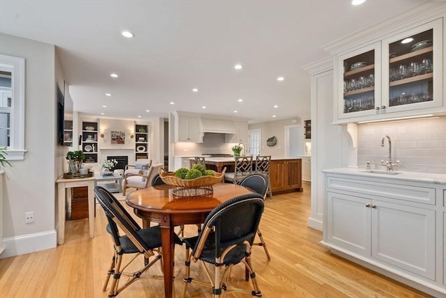 dining room with a fireplace, light wood finished floors, recessed lighting, wet bar, and baseboards