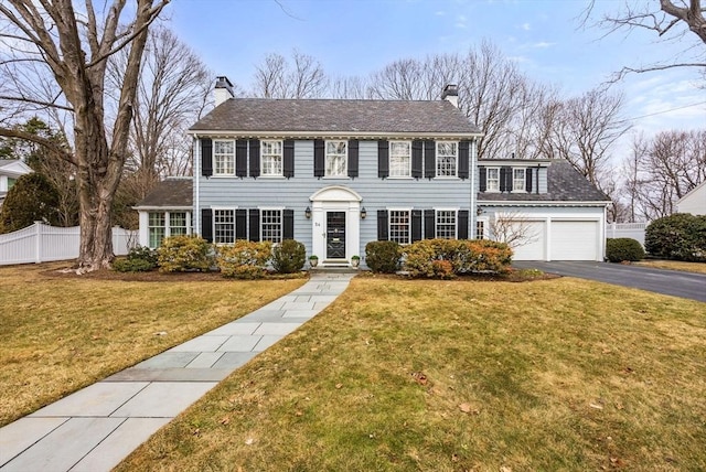 colonial home with a front lawn, fence, a chimney, and an attached garage