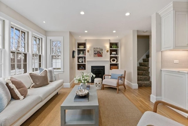 living area featuring recessed lighting, a fireplace, light wood-style flooring, and stairs