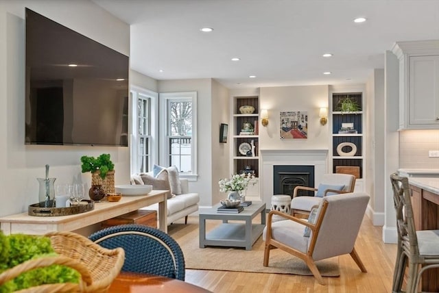 living room featuring light wood finished floors, a fireplace, baseboards, and recessed lighting