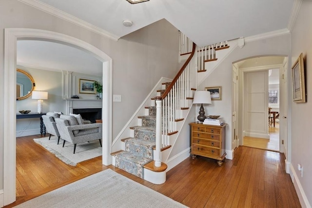 stairs featuring a fireplace, arched walkways, hardwood / wood-style floors, and ornamental molding