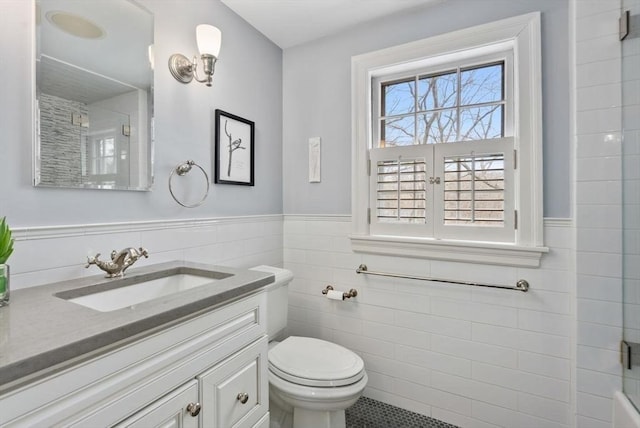 bathroom featuring toilet, a wainscoted wall, vanity, tile walls, and a shower