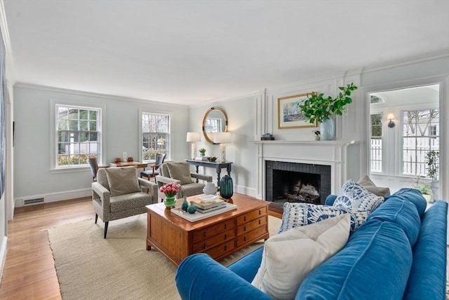 living area featuring crown molding, a fireplace, light wood finished floors, visible vents, and baseboards