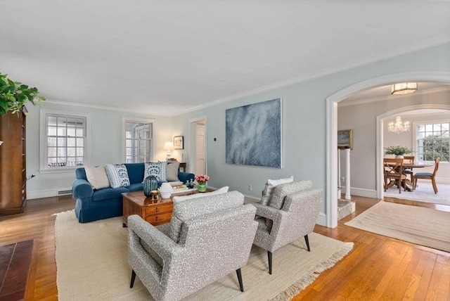 living room featuring arched walkways, a notable chandelier, wood finished floors, baseboards, and crown molding