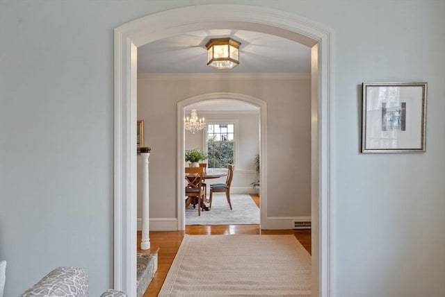 hall featuring arched walkways, visible vents, ornamental molding, wood finished floors, and baseboards