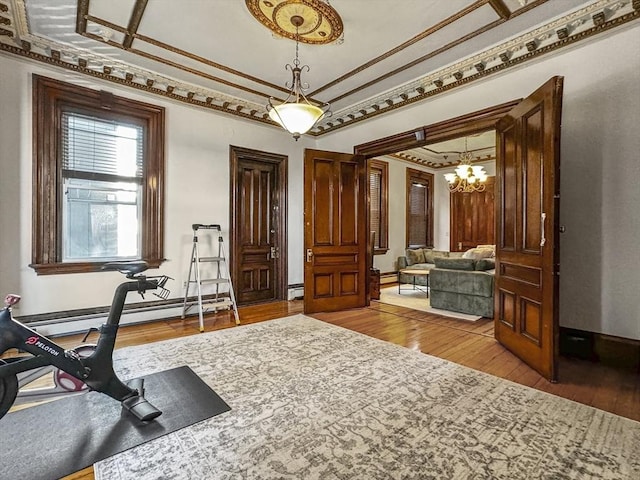 exercise room featuring a baseboard radiator, a chandelier, ornamental molding, and hardwood / wood-style flooring