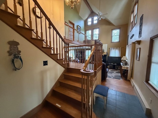 staircase featuring a high ceiling, ceiling fan with notable chandelier, a baseboard heating unit, and wood-type flooring