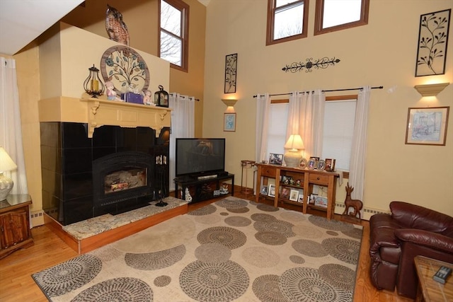 living room with hardwood / wood-style flooring, a high ceiling, a tile fireplace, and a baseboard radiator