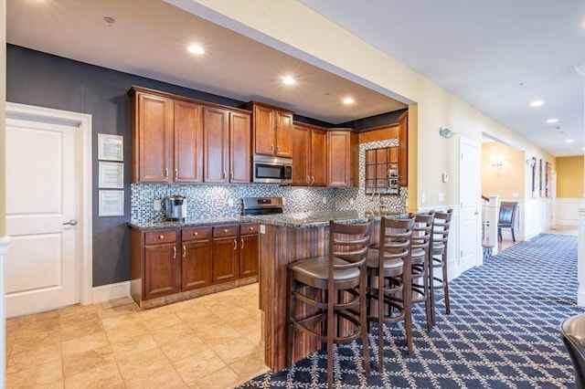 21 Cielo Dr, Dover, NH 03820 - kitchen with stainless steel appliances, brown cabinets, a kitchen bar, tasteful backsplash, and dark stone counters