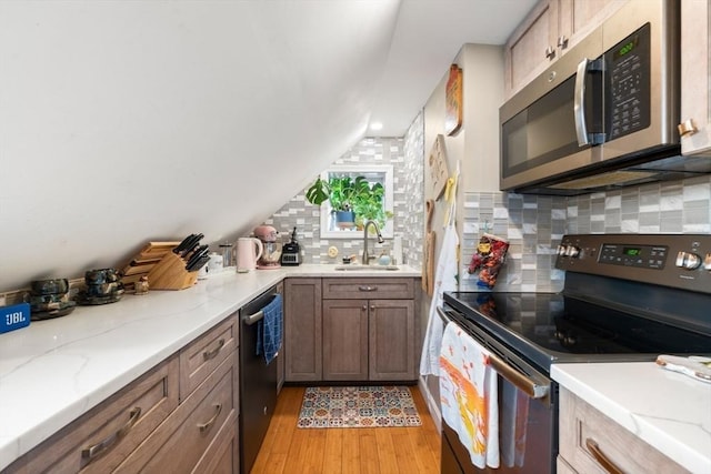 kitchen with appliances with stainless steel finishes, sink, light stone counters, and light hardwood / wood-style flooring