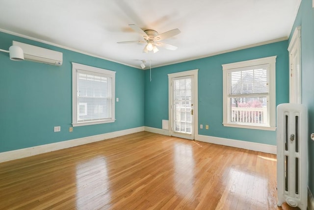 empty room with ornamental molding, ceiling fan, radiator heating unit, a wall unit AC, and light wood-style flooring