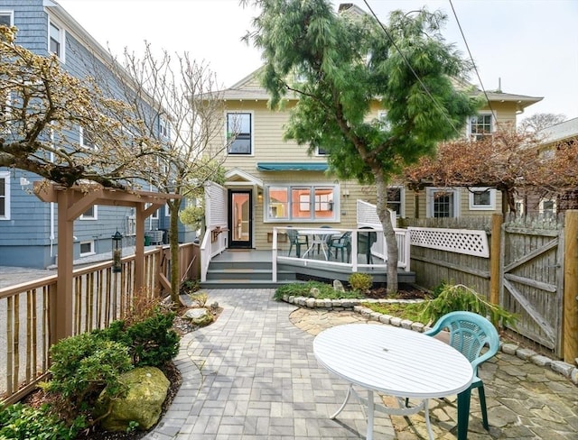 rear view of property with fence, a wooden deck, and a patio area