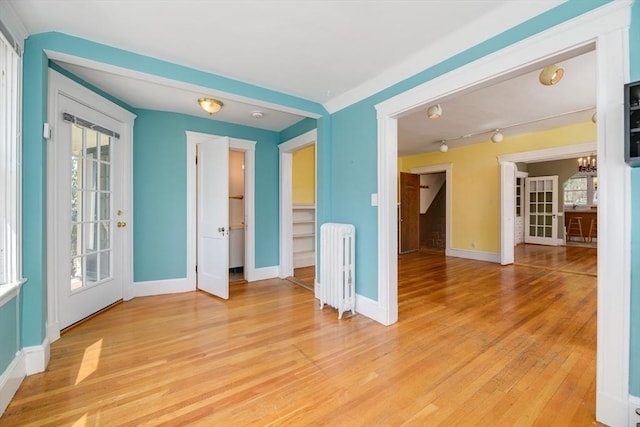 unfurnished room with baseboards, radiator, light wood finished floors, and a wealth of natural light