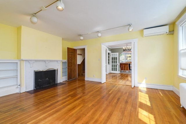 unfurnished living room with track lighting, a notable chandelier, an AC wall unit, and a fireplace