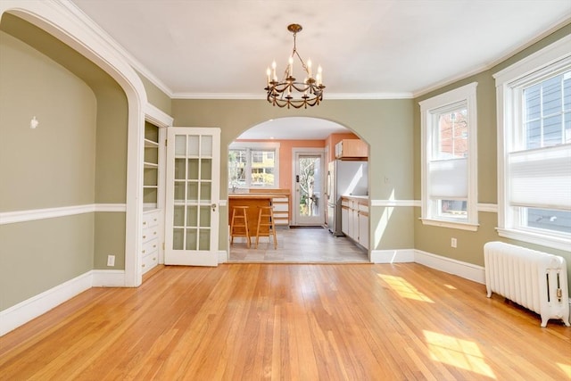 unfurnished dining area with radiator, baseboards, a chandelier, arched walkways, and light wood-style flooring