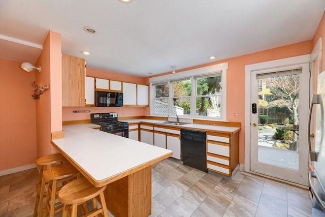 kitchen with a peninsula, a breakfast bar, light countertops, a sink, and black appliances