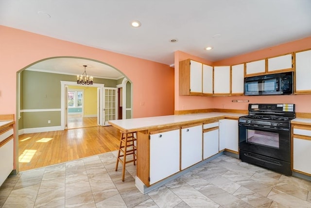 kitchen featuring a notable chandelier, light countertops, arched walkways, a peninsula, and black appliances