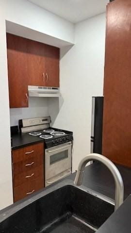 kitchen featuring stainless steel range with gas cooktop, brown cabinetry, under cabinet range hood, a sink, and dark countertops
